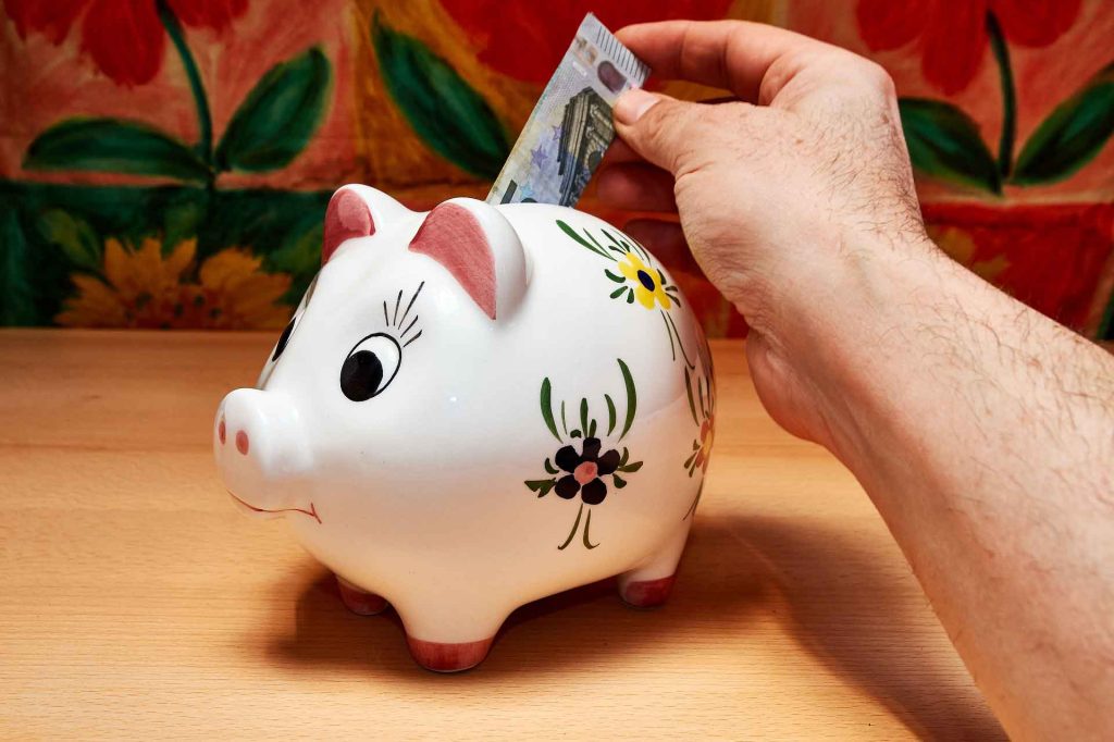 A hand inserting a currency note in a white piggy savings bank