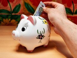A hand inserting a currency note in a white piggy savings bank