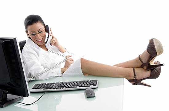 woman sitting at office desk with feet on table and chatting on phone