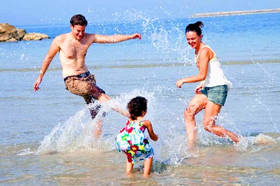 Father, mother, and little daughter playing on beach and having holiday fun