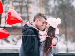 A couple in love standing close with nose touching and red heart balloons in hand