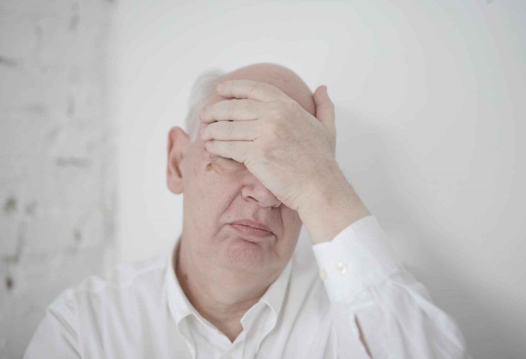 An elderly man in depression covering his head by hand