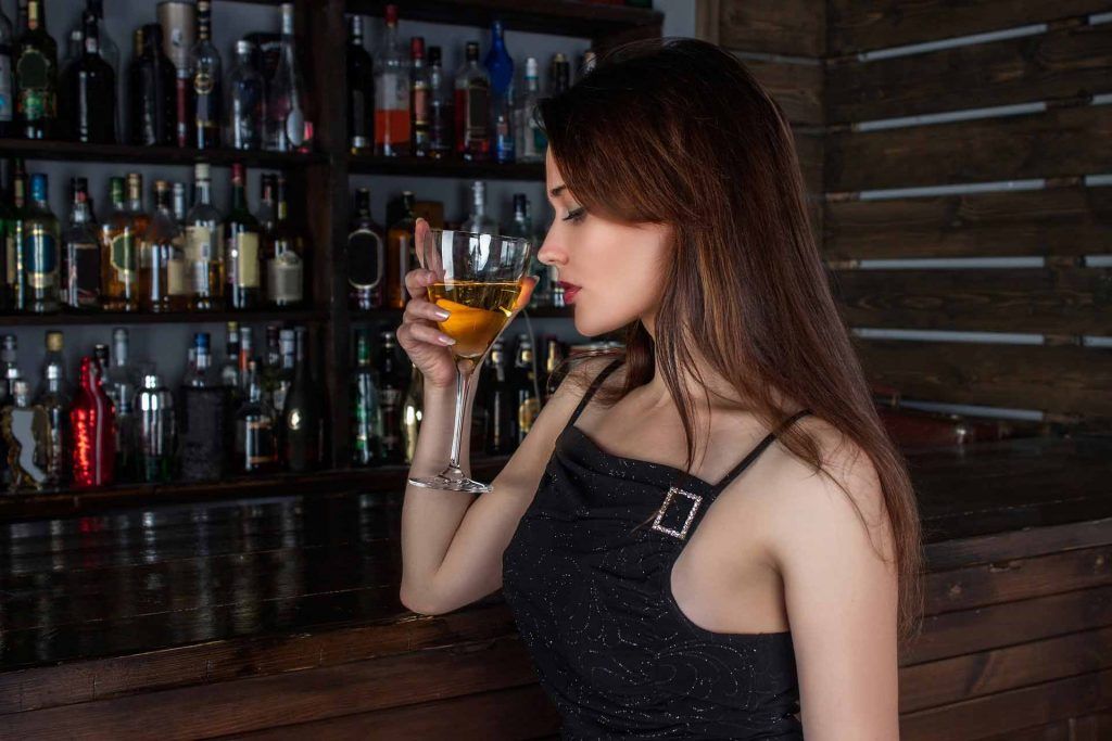 Girl struggling with alcohol addiction drinking in a bar