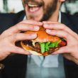 Man eating burger with hands to satisfy hunger or appetite