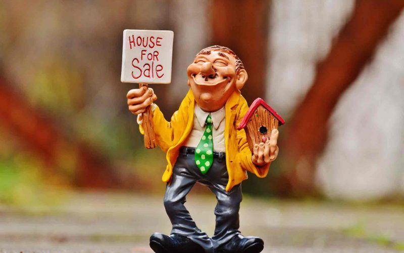 An animated man with house model and placard in hand trying to sell his house