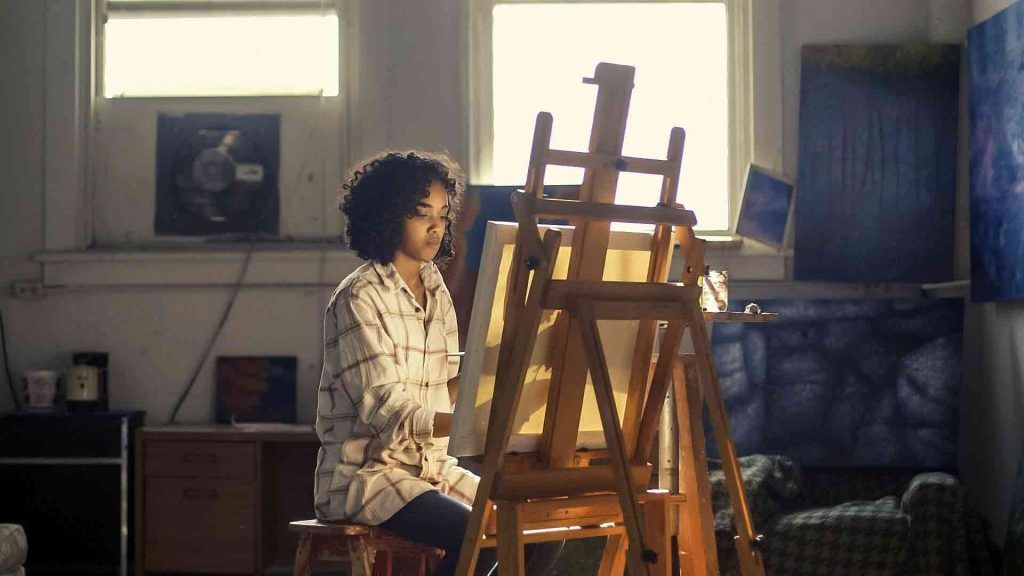 A girl painting on a canvas placed on an easel as a hobby