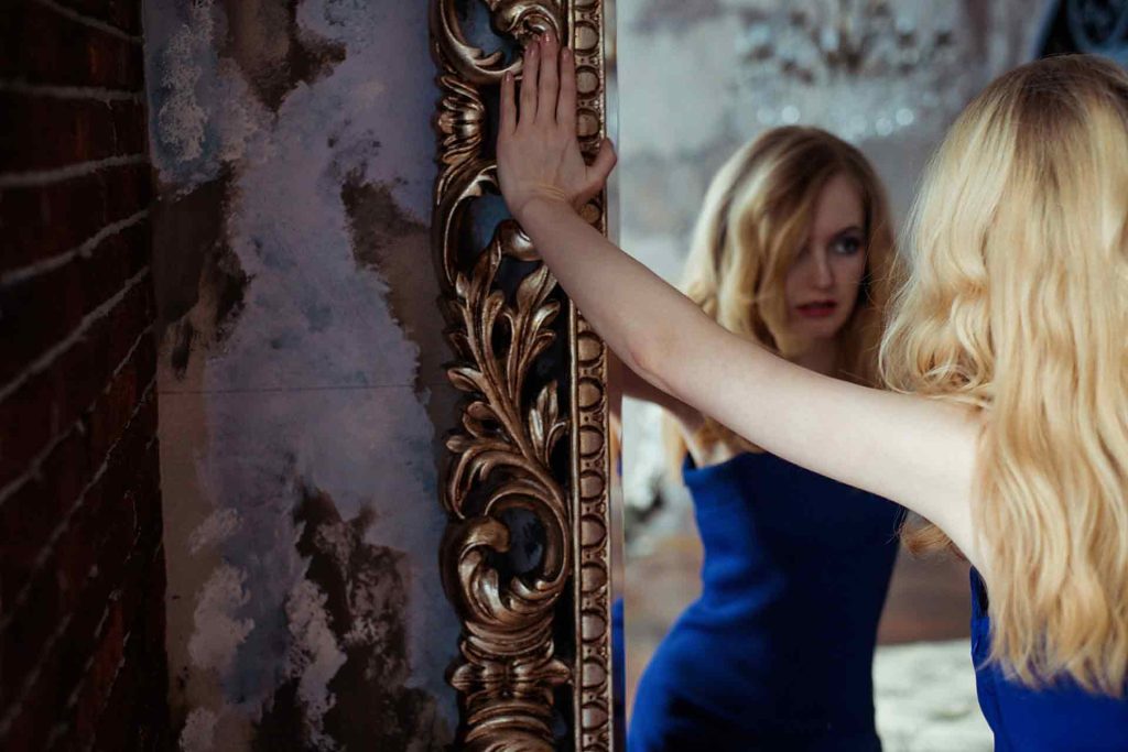 A blonde narcissist woman standing and viewing herself in a mirror