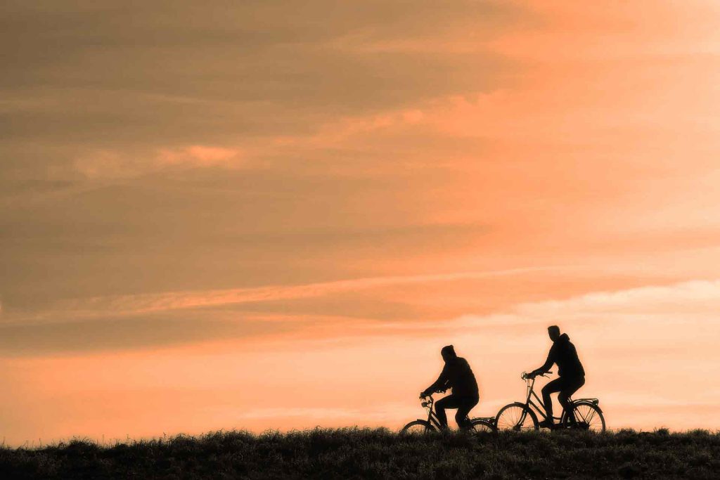 Silhouette of two men cycling against the sunset.