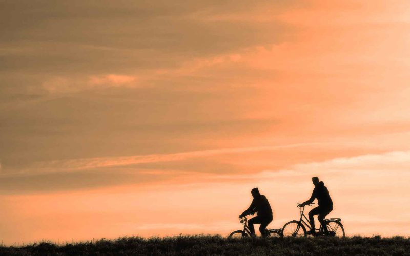 Silhouette of two men cycling against the sunset.